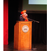 A lady with a red hat speaking at the podium