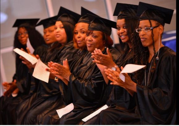 women in caps and gowns clapping while at graduation ceremony