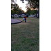 A child with a red shirt on and a red helmet, pushing a bicycle on the grass