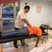 A man in an orange shirt laying on a massage table with a man massaging his back