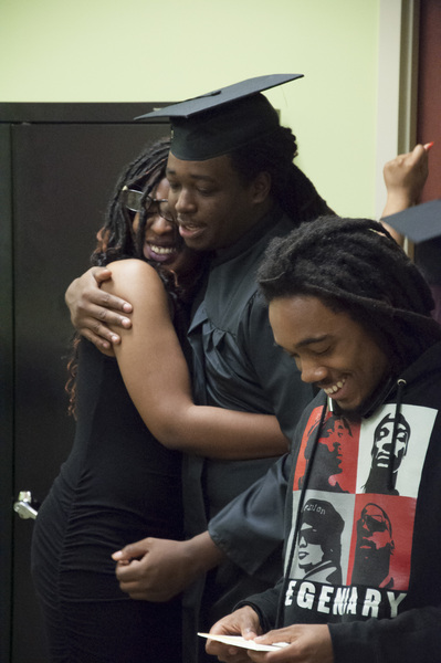 A man wearing a cap and gown embracing a young woman with a man smiling next to them