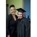 A smiling lady in a black dress standing next to a student in a cap and gown with red hair
