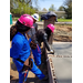 Two girls wearing pink hard hats listen to instruction on smoothing the concrete from the Contractor
