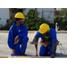 Two young males wearing yellow hard hats and blue jumpsuits framing