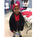 A little boy wearing a red stocking hat with a black jacket with a black and red vest under it and red gloves
