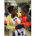A mother holding a child in his brand new orange and black coat and holding a stuffed snowman